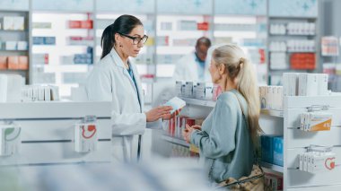 Eczane: Profesyonel Kafkasyalı Eczacı Güzel Yaşlı Kadın Müşteriye Tıbbi Tavsiye, Tavsiye ve Konuşmayla Yardım Ediyor. İlaç, hap, sağlık hizmeti ve güzellik ürünleriyle dolu bir eczane.