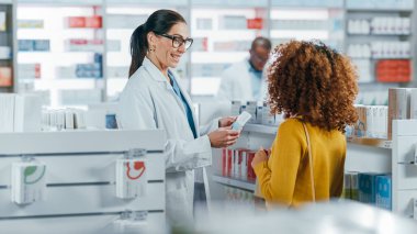 Eczane: Profesyonel Kafkasyalı Eczacı Güzel Siyahi Kadın Müşteriye Tıbbi Tavsiye, Tavsiye ve Konuşmayla Yardım Ediyor. İlaç, hap, sağlık hizmeti ve güzellik ürünleriyle dolu bir eczane.