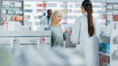 Eczane: Profesyonel Kafkasyalı Eczacı Güzel Yaşlı Kadın Müşteriye Tıbbi Tavsiye, Tavsiye ve Konuşmayla Yardım Ediyor. İlaç, hap, sağlık hizmeti ve güzellik ürünleriyle dolu bir eczane.