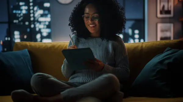 美丽而真实的拉丁女性坐在舒适的夜晚黑暗客厅沙发沙发沙发上 在家中使用平板电脑 她在上网 用Stylus铅笔写作和画画 — 图库照片