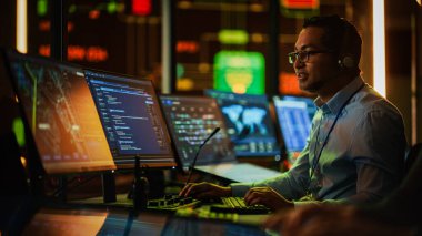 Profesyonel IT Teknik Destek Uzmanı ve Yazılım Geliştiricisi Dijital Ekranlarla Bilgisayar Kontrol Odasında çalışıyor. Çalışan Mikrofonlu Kulaklık Kullan ve Konuşurken Çağrı Yap.
