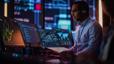Profesyonel IT Teknik Destek Uzmanı ve Yazılım Geliştiricisi Dijital Ekranlarla Bilgisayar Kontrol Odasında çalışıyor. Çalışan Mikrofonlu Kulaklık Kullan ve Konuşurken Çağrı Yap.