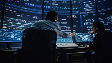 Profesyonel IT Teknik Destek Uzmanı ve Yazılım Geliştiricisi Dijital Ekranlarla Bilgisayar Kontrol Odasında çalışıyor. Çalışan Mikrofonlu Kulaklık Kullan ve Konuşurken Çağrı Yap.