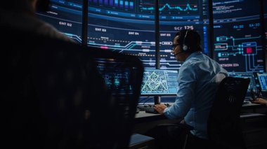 Profesyonel IT Teknik Destek Uzmanı ve Yazılım Geliştiricisi Dijital Ekranlarla Bilgisayar Kontrol Odasında çalışıyor. Çalışan Mikrofonlu Kulaklık Kullan ve Konuşurken Çağrı Yap.