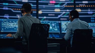 Profesyonel IT Teknik Destek Uzmanı ve Yazılım Geliştiricisi Dijital Ekranlarla Bilgisayar Kontrol Odasında çalışıyor. Çalışan Mikrofonlu Kulaklık Kullan ve Konuşurken Çağrı Yap.