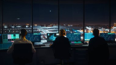 Çeşitli Hava Trafik Kontrol Ekibi gece modern havaalanı kulesinde çalışıyor. Ofis Odası Masaüstü Bilgisayarı ile dolu Navigasyon Ekranları, Uçak Gidiş ve Denetleyiciler için Gelen Veri.