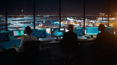 Çeşitli Hava Trafik Kontrol Ekibi gece modern havaalanı kulesinde çalışıyor. Ofis Odası Masaüstü Bilgisayarı ile dolu Navigasyon Ekranları, Uçak Gidiş ve Denetleyiciler için Gelen Veri.