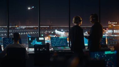 Gece Havalimanı Kulesi 'nde Kulaklıklı Kadın ve Erkek Hava Trafik Kontrolörleri. Ofis Odası Masaüstü Bilgisayarı ile dolu Navigasyon Ekranları, Kontrol Edenler için Uçak Uçuş Radar Verisi.