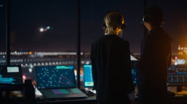 Gece Havalimanı Kulesi 'nde Kulaklıklı Kadın ve Erkek Hava Trafik Kontrolörleri. Ofis Odası Masaüstü Bilgisayarı ile dolu Navigasyon Ekranları, Kontrol Edenler için Uçak Uçuş Radar Verisi.