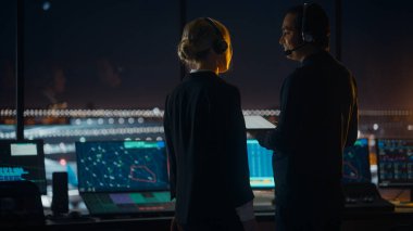 Gece Havalimanı Kulesi 'nde Kulaklıklı Kadın ve Erkek Hava Trafik Kontrolörleri. Ofis Odası Masaüstü Bilgisayarı ile dolu Navigasyon Ekranları, Kontrol Edenler için Uçak Uçuş Radar Verisi.