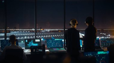 Gece Havalimanı Kulesi 'nde Kulaklıklı Kadın ve Erkek Hava Trafik Kontrolörleri. Ofis Odası Masaüstü Bilgisayarı ile dolu Navigasyon Ekranları, Kontrol Edenler için Uçak Uçuş Radar Verisi.