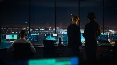 Gece Havalimanı Kulesi 'nde Kulaklıklı Kadın ve Erkek Hava Trafik Kontrolörleri. Ofis Odası Masaüstü Bilgisayarı ile dolu Navigasyon Ekranları, Kontrol Edenler için Uçak Uçuş Radar Verisi.