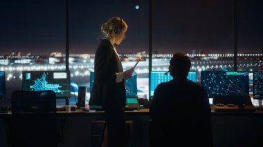 Gece Havalimanı Kulesi 'nde Kulaklıklı Kadın ve Erkek Hava Trafik Kontrolörleri. Ofis Odası Masaüstü Bilgisayarı ile dolu Navigasyon Ekranları, Kontrol Edenler için Uçak Uçuş Radar Verisi.