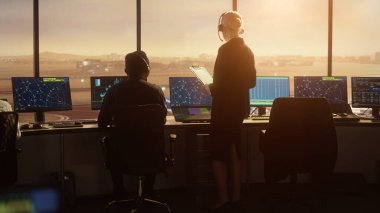 Havaalanı kulesinde Kulaklık takan Kadın Hava Trafik Kontrolörü. Ofis odası, Takım için Uçak Uçuş Radar Verisi, Navigasyon Ekranları ve Masaüstü Bilgisayarlarıyla dolu.
