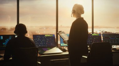 Havaalanı kulesinde Kulaklık takan Kadın Hava Trafik Kontrolörü. Ofis odası, Takım için Uçak Uçuş Radar Verisi, Navigasyon Ekranları ve Masaüstü Bilgisayarlarıyla dolu.