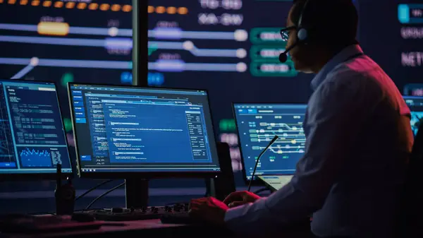 Profesyonel IT Teknik Destek Uzmanı ve Yazılım Geliştiricisi Dijital Ekranlarla Bilgisayar Kontrol Odasında çalışıyor. Çalışan Mikrofonlu Kulaklık Kullan ve Konuşurken Çağrı Yap.