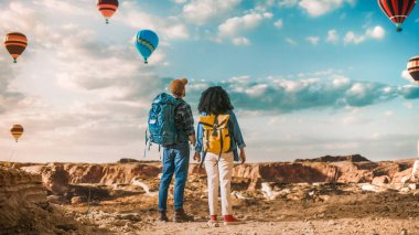 Rocky Canyon Vadisi 'nde sırt çantalı genç turist çift yürüyüşü. Macera Gezisinde Erkek ve Kadın El ele tutuşuyor. Mountain National Park 'ta Sıcak Hava Balonu Festivali.