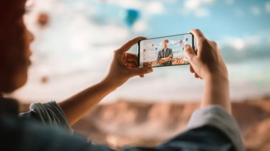 Heyecanlı Genç Çok Irklı Gezgin Afro Saç Tarzı ile Rocky Canyon Vadisi 'nde Erkek arkadaşının Akıllı Telefon Fotoğrafını Çekiyor. Mountain National Park 'ta Sıcak Hava Balonu Festivali.