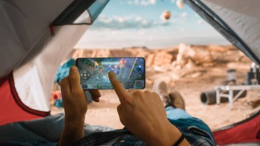 Arcade Mobil Oyunu oynamak için akıllı telefon kullanan bir turistin POV 'u, Ekrandan Parmak Siliyorum. Gezgin Rocky Dağı 'nın tepesindeki çadırda dinleniyor ve Uçan Sıcak Hava Balonları.
