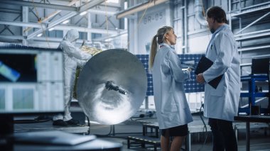 Mühendis ve Teknisyen Konuşması, Uydu İnşaatı üzerinde çalışırken Tablet Bilgisayar kullanın. Uzay Ajansı İmalat Tesisi: Bilim adamları Uzay Keşif Görevi İçin Uzay Aracı İnşa Ediyor, Birleştiriyor