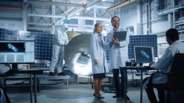 Happy Engineer and Technician Talk, uydu inşaatı üzerinde çalışırken dizüstü bilgisayar kullanın. Uzay Ajansı Üretim Tesisi: Bilim adamları Uzay Keşif Görevi için Uzay Aracı Kurdular