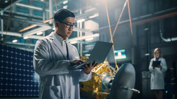 Industrial Engineer Working on Artificial Satellite Construction. Aerospace Agency: Asian Scientist Using Laptop Computer to Develop Spacecraft for Space Exploration and Data Communication.