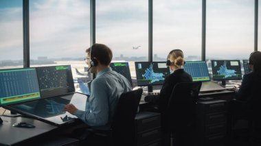 Modern bir havaalanı kulesinde çalışan çeşitli hava trafik kontrol ekibi. Ofis Odası, Kontrol Edenler için Uçak Uçuş Radar Verisi, Navigasyon Ekranlarıyla Masaüstü Bilgisayarı ile Doludur.