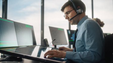 Havalimanı Kulesi 'nde Kulaklık Konuşması yapan Erkek Hava Trafik Kontrolörü. Ofis Odası, Takım için Navigasyon Ekranları, Uçak Gidiş ve Gelen Veri ile Masaüstü Bilgisayarı ile Doludur.