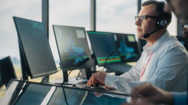 Havalimanı Kulesi 'ndeki Dokunmatik Ekran Masa Paneli ile Erkek Hava Trafik Kontrolörü. Ofis, Navigasyon Ekranlı, Uçak Gidiş ve Takıma Veri Gelen Bilgisayarlarla dolu..