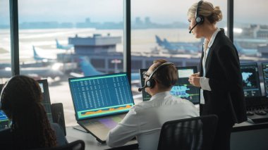 Havalimanı Kulesi 'nde Kulaklıklı Kadın ve Erkek Hava Trafik Kontrolörleri. Ofis odası, Takım için Uçak Uçuş Radar Verisi, Navigasyon Ekranları ve Masaüstü Bilgisayarlarıyla dolu.