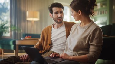 Çift, dairelerinin oturma odasında otururken dizüstü bilgisayar kullanıyor. Erkek Arkadaş ve Kız Arkadaş Konuşur, İnternetten Alışveriş yapar, İnternetten Sipariş Vermek İçin Ürün Seçer, Video İzler