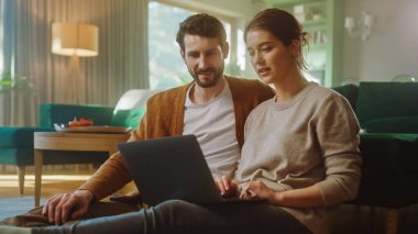 Çift, dairelerinin oturma odasında otururken dizüstü bilgisayar kullanıyor. Erkek Arkadaş ve Kız Arkadaş Konuşur, İnternetten Alışveriş yapar, İnternetten Sipariş Vermek İçin Ürünü Seçer, Birlikte Uzaktan Çalışıyor