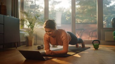 Güzel Kız Evde Egzersiz Yapıyor, Dizüstü bilgisayarda Ders İzliyor. Otantik Artı Boyutlu Kadın Spor Yapıyor, Spor Antrenmanı, Plank, Gergin Yoga Egzersizleri. Güneşli Şık Oturma Odası