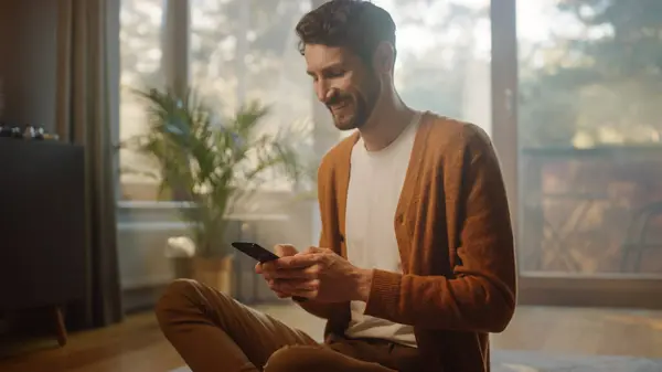 Mann Som Bruker Smarttelefon Hjemme Virker Fjernstyrt Handsome Smiling Male – stockfoto