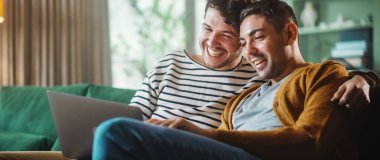 Konforlu Moda Apartmanında Kanepede otururken Dizüstü bilgisayar kullanan Nazik Gay Çiftin Portresi. Yetişkin Erkek Arkadaşları İnternet 'te Alışveriş, Canlı Servis' te Komik Videolar İzleme.