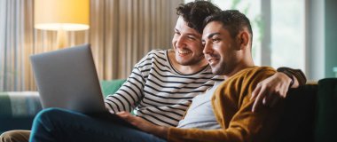 Konforlu Moda Apartmanında Kanepede otururken Dizüstü bilgisayar kullanan Nazik Gay Çiftin Portresi. Yetişkin Erkek Arkadaşları İnternet 'te Alışveriş, Canlı Servis' te Komik Videolar İzleme.
