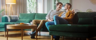 Mutlu Gay bir çiftin portresi TV izlerken, rahat bir dairede bir koltukta oturuyor. Yetişkin Erkek Arkadaşlara Sarılma, Komik Videolar İzleme ve Çevrimiçi Servisten Yayın Filmleri.