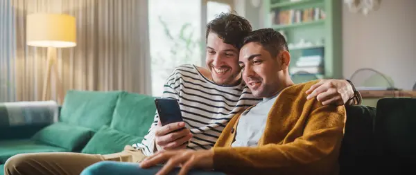 Muotokuva Gentle Gay Pari Älypuhelimella Kun Istuu Sohvalla Viihtyisässä Tyylikkäässä — kuvapankkivalokuva