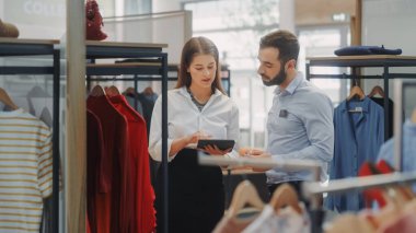 Giyim Mağazası: İş kadını Tablet Bilgisayar kullanıyor, Görsel Ticaret Uzmanıyla konuşuyor, Moda Koleksiyonu Yaratmak İçin İşbirliği yapıyor. Küçük İşletme Moda Mağazası Satış Müdürü Tasarımcıyla Konuşuyor