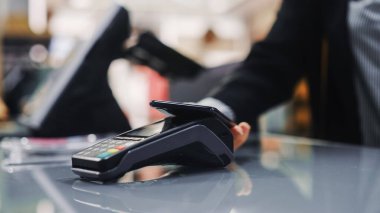 Giyim mağazası: Tezgahtaki Kadın, Smartphone vasıtasıyla, Temassız NFC Terminalinden Kıyafet Aldı. Alışveriş merkezi, alışveriş merkezi, alışveriş merkezi. Cep telefonuna odaklan