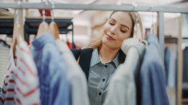 Gülümseyen Güzel Kadın Müşteri Alışveriş Mağazasında, Şık Kıyafetler Seçme, Bluz Seçme, Gömlek Seçme. Moda Dükkanındaki Kız, Sürdürülebilir Marka Tasarımları, Yeni Koleksiyon. Yakın plan.