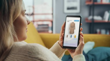 Güzel Beyaz Kadın, New Collection 'dan Elbise Seçip Almak İçin İnternet Mağazası ile Akıllı Telefon Kullanıyor. İnternette Sörf Yapan ve Oturma Odasında Kanepede Yatan Kadın.
