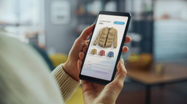 Güzel Beyaz Kadın, New Collection 'dan Ceket Seçip Satın Almak İçin İnternet Mağazası ile Akıllı Telefon Kullanıyor. İnternette Sörf Yapan ve Oturma Odasında Kanepede Yatan Kadın.