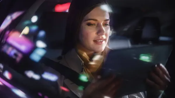 时尚的女性晚上在出租车后座上换车回家 城市街道上的漂亮女性乘客在开车时用平板电脑 车上有工作霓虹灯的标志 — 图库照片