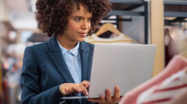 Giyim Mağazası: Kadın Ticaret Yöneticisi Moda Koleksiyonu oluşturmak için dizüstü bilgisayar kullanıyor. Profesyonel Satış Perakende Asistan Çekleri. Küçük İşletme Sahibi Alışveriş Merkezi Ögeleri Siparişi Verdi.