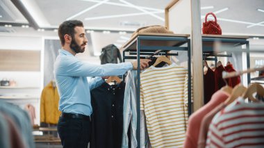 Yakışıklı Erkek Giyim Mağazası Moda Alışveriş Merkezi 'nde Çalışan Asistanı. Profesyonel Mağaza Satış Perakende Yardımcısı, Sürdürülebilir Günlük Tasarım Raflarında Yeni Renkli Koleksiyonu Asıyor.