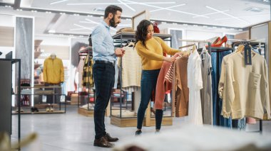 Genç Bayan Müşteri Alışverişi Giyim Mağazasından, Perakende Satış Ortaklığı Danışmanlığa Yardım Ediyor. Moda Mağazasında Çeşitli İnsanlar, Şık Kıyafetler Seçmek, Sürdürülebilir Tasarımlı Renkli Markalar