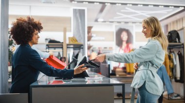 Giyim Mağazası Veznedar Tezgâhı: Kadın ve Erkek Perakende Yöneticileri, Yeni Moda Giysiler İçin Genç Stil Bir Kadın Müşteriden NFC Akıllı Telefon Ödemesini Kabul Etti.