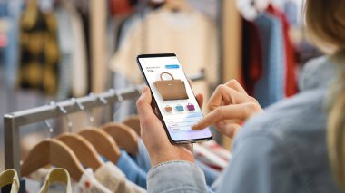 Giysi Mağazası: Moda Mağazası Online Kullanıcı Arayüzü ile Smartphone Kullanan Kadın Moda Ürünleri. Mobil Aygıtın Omuz Çekiminin Üstünü Kapat.