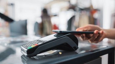 Giyim Mağazası: Tezgâhtaki müşteri, Temassız NFC Bank Terminali aracılığıyla Smartphone ile Kıyafet Ödeme yapıyor. Şık Tasarımcı Markaları ile Moda Dükkanı. Yakından El 'e Odaklan.